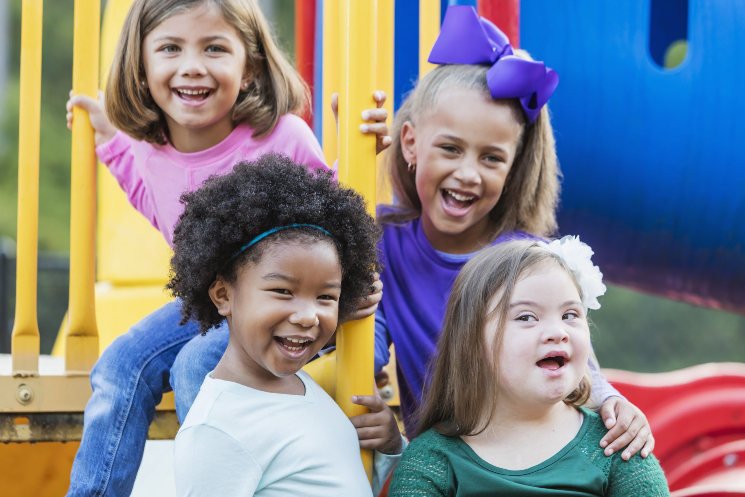 image: a group of diverse girls in a play park setting, one with obvious disabilities