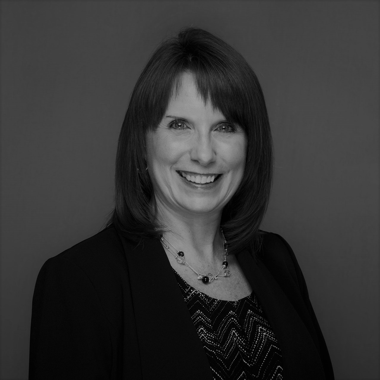 image: a black and white headshot of a woman in business attire looking at the camera