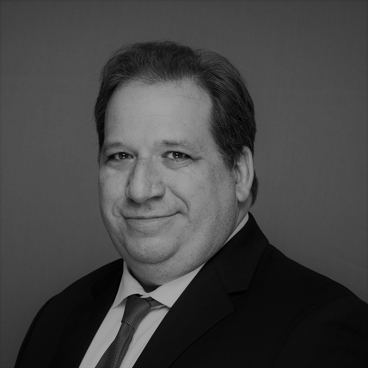 image: a black and white headshot of a man in business attire looking at the camera