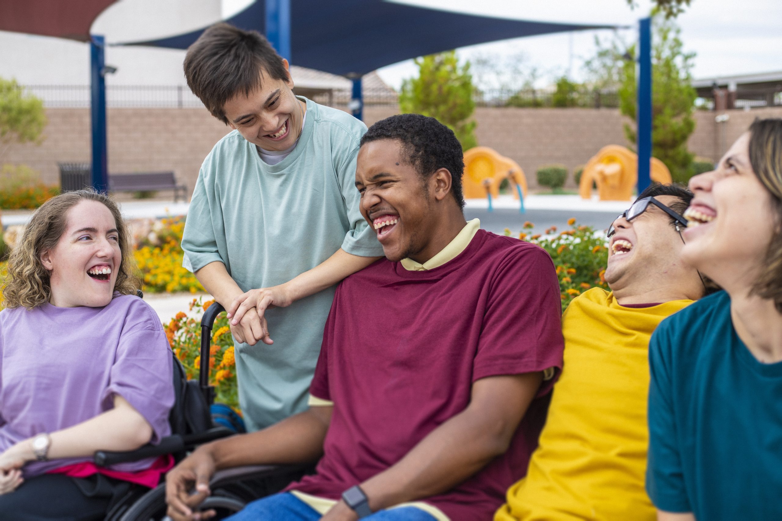 image: a group of diverse friends all with obvious disabilities laughing with each other at an outside setting